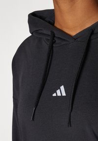 Fato preto com capuz, apresentando um bolso canguru na frente, logótipo branco de três riscas no peito, cordões ajustáveis e tecido de algodão suave.