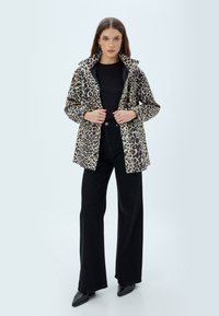 Jakke med leopardprint, krave og knaplukning, lavet af letvægtsstof. Bæres over en sort bluse og parret med sorte bukser i vidde.