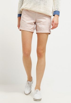 Pantalones cortos de algodón rosa claro, con puños enrollados, combinados con zapatillas blancas. La parte superior es un suéter de punto suelto en color crema con una capa inferior de mezclilla.