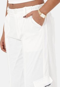 Witte cargobroek met een elastische tailleband, zijzakken en een merketiket. De stof heeft een gladde textuur en een casual ontwerp.