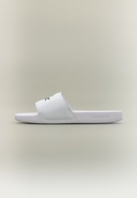 White slide sandal with a wide strap featuring a green logo. The sole is flat and light, made from synthetic material with a smooth finish.