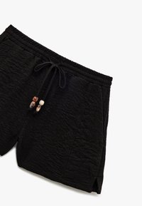 Zwarte textured shorts met elastische tailleband en koord, versierd met vier decoratieve bruine en beige kralen.
