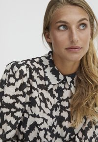 Camicia a motifs in bianco e nero con colletto, texture plissettata e chiusura a bottoni. Presenta una vestibilità ampia e dettagli in tessuto testurizzato.