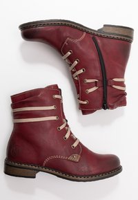 Røde læder ankelstøvler med rund tå, snørebånd foran og lynlås i siden. Har beige snørebånd og brun struktureret hæl som accent.
