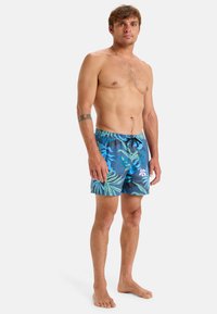 Niebieskie kąpielówki z tropikalnym wzorem liści w odcieniach zieleni i różu. Wykonane z lekkiego materiału, z elastycznym pasem i sznurkiem do regulacji.