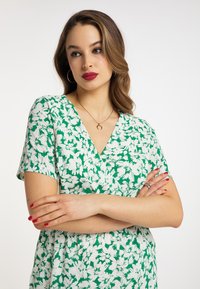 Grön blommig klänning med korta ärmar, med en djup V-ringning och en luftig design. Materialet är lättviktigt med en slät textur.