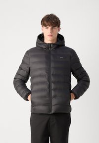 Giubbotto piumino nero con cappuccio, caratterizzato da cuciture orizzontali, una zip frontale e un piccolo logo sul petto. Materiale liscio e isolante.