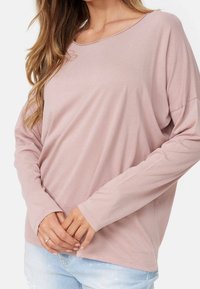 Helles rosa Langarmoberteil mit lockerer Passform, weitem Rundhalsausschnitt, weichem Material und genähtem Saum. Kombiniert mit hellblauen, ausgebeulten Jeans.