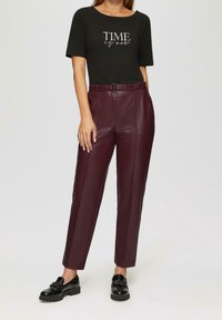 Svart t-shirt med vit text, kombinerad med högmidjade bordeauxfärgade byxor i konstläder och svarta lackskor. Rena linjer och modern passform.