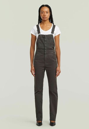 Donkergrijze overalls met verstelbare bandjes, voorzakken en een aansluitend ontwerp, gecombineerd met een witte t-shirt en zwarte schoenen.
