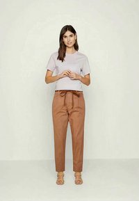 Camisa curta de manga curta lilás clara combinada com calças altas castanhas e sandálias de tiras em tom de areia, com um detalhe de cintura amarrada.