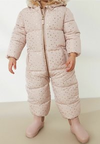Un mono acolchado de color rosa claro con patrones de estrellas doradas, cremallera en la parte delantera y capucha con pelo. Combinado con botas de goma rosas a juego.