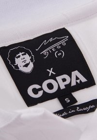 Witte stoffen shirtslabel met zwarte branding, een portretomtrek en tekst: "COPA x DIEGO," met "Made in Europe" in kleine letters. Maat S.