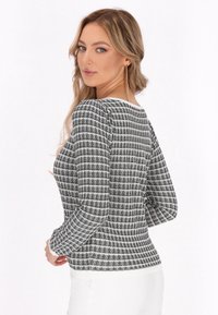 Fekete-fehér kockás, hosszú ujjú felső, kerek nyakkal, textúrált anyagból, testhezálló szabással. Hátulról látható a ráncolt vállrész.