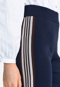 Pantalones deportivos azul marino con un acabado texturizado. Presentan franjas marrones y blancas a lo largo de los costados y una cintura acanalada.