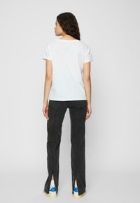 White short-sleeve t-shirt paired with black flared pants featuring slits at the hem. The pants have a subtle textured finish.