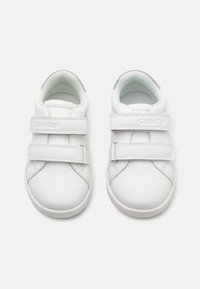 Baskets en cuir blanc avec deux bandes Velcro, bout rond, intérieur rembourré et logo discret sur le côté.