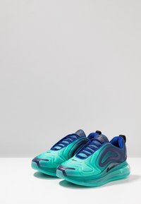 Aqua a námořnicky modrá teniska s vlnitým designem, hladkým vnějším materiálem, viditelným šněrováním a průhlednou podrážkou. Má výrazné logo Nike.