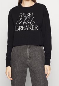 Felpa nera cropped con maniche lunghe, caratterizzata da un testo bianco che recita "REBEL & Rule BREAKER". Design semplice, tessuto morbido.