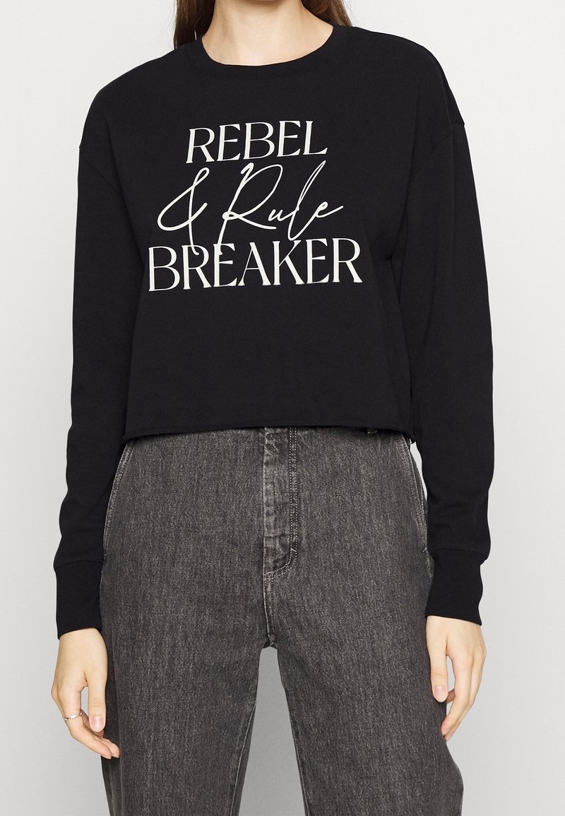 Felpa nera cropped con maniche lunghe, caratterizzata da un testo bianco che recita "REBEL & Rule BREAKER". Design semplice, tessuto morbido.