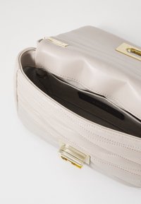 Borsa a tracolla in pelle avorio chiaro con design trapuntato, hardware dorato e chiusura magnetica. L'interno presenta una fodera in tessuto e una tasca a scomparsa.