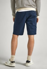 Shorts en coton bleu marine à coupe droite, avec deux poches arrière et une texture lisse, associés à des baskets blanches et des chaussettes beiges.