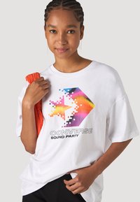 Camiseta de algodón blanca con un gráfico de estrella arcoíris pixelada y el texto "CONVERSE SOUND PARTY". Manga corta y ajuste relajado.