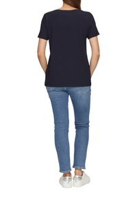 Marineblauwe t-shirt met korte mouwen, van katoen, relaxte pasvorm, gecombineerd met lichtblauwe jeans en zilveren sneakers, gezien vanuit de achterkant.