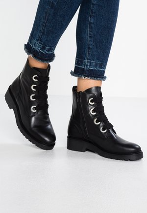 Mustat nahkaiset nilkkurit, joissa paksut mustat nauhat, sivuvetoketju ja paksupohjaiset pohjat. Kenkäparia käytetty tummansinisten revittyjen farkkujen kanssa.