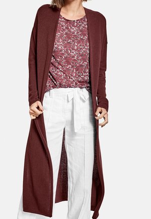 Long cardigan bordeaux en tissu doux, ouvert à l'avant, assorti à un haut à motifs rouges et blancs, et un pantalon blanc avec une taille nouée.
