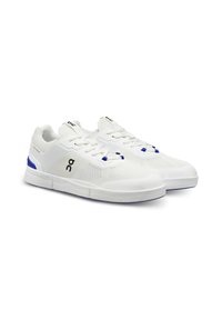 Zapatillas deportivas blancas con parte superior de malla, acentos azules y suela plana. Presentan cordones tradicionales y una superficie texturizada para mayor agarre.