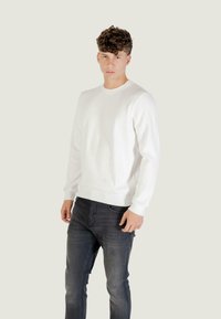 Witte geribde langemouwen trui met een ronde hals, gecombineerd met donkergrijze slim-fit jeans. Zachte textuur, aansluitend ontwerp, minimalistische stijl.