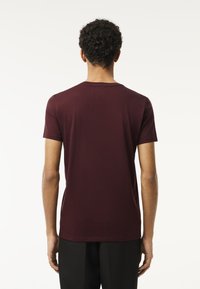 Burgundy lyhythihainen t-paita sileästä, kevyestä kankaasta, jossa on pyöreä kaula-aukko ja istuva siluetti.