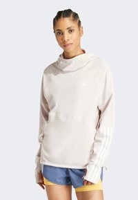 Sweatshirt à capuche rose clair avec une texture douce, arborant des accents tricolores blancs sur les manches et un design à coupe décontractée.
