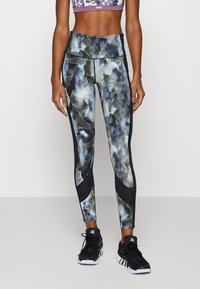 Černé a multicolor legíny s abstraktními vlnitými vzory, vysokým pasem a kontrastními černými bočními panely. V kombinaci s černými teniskami.