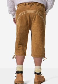 Brune suede shorts i knælængde med en bundet kant, to lommer og broderet detalje langs ryggen. Bæres med beige strømper og brune støvler.