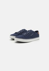 Marineblaue Leinensneaker mit weißen Gummisohlen, runder Spitze, flachen Schnürsenkeln und einem Akzent aus braunem Leder an der Ferse.