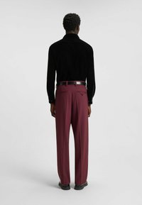 Schwarzes Cordhemd mit Kragen und Manschetten, kombiniert mit burgunderroten, maßgeschneiderten Hosen und einem schwarzen Gürtel. Glatte Textur mit dezentem Glanz.