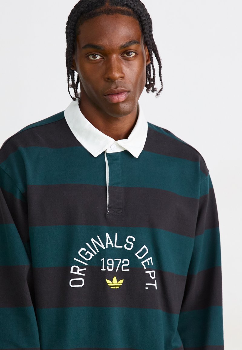 T-shirt de rugby rayé noir et vert foncé avec un col blanc, arborant "ORIGINALS DEPT. 1972" et un logo jaune sur la poitrine.