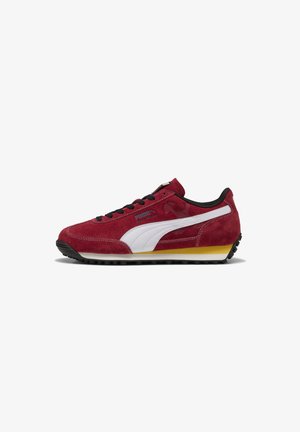 Baskets en nubuck rouge avec des accents noirs, rayure latérale blanche, semelle en caoutchouc et lacets noirs. Présente un petit détail de marque sur le côté.