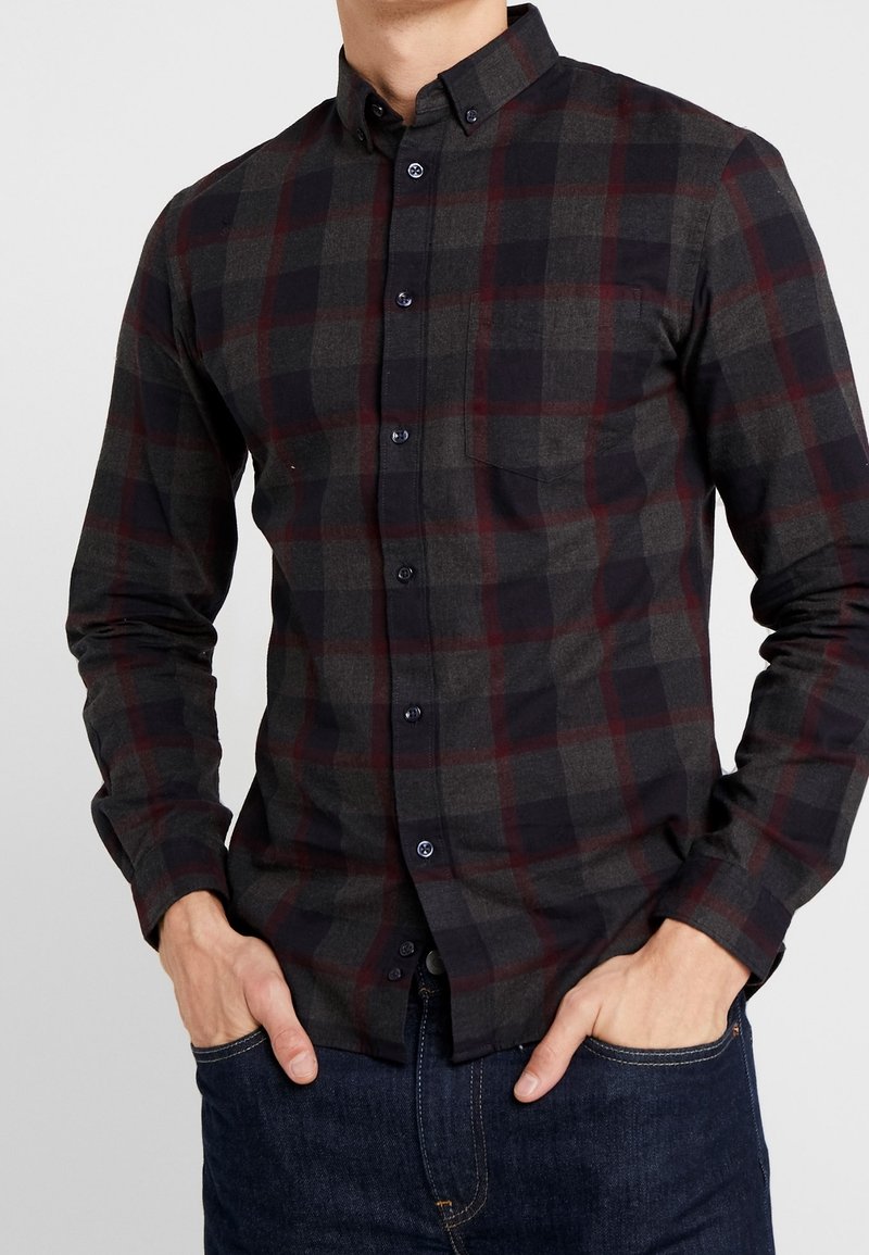 Camicia a bottoni a quadri in grigio scuro, rosso e nero. Presenta maniche lunghe, colletto e taschino sul petto. Realizzata in tessuto testurizzato.