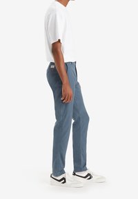 Blå bomullsbyxor med rak bendesign, i kombination med en vit t-shirt med kort ärm och vita sneakers med svarta detaljer.