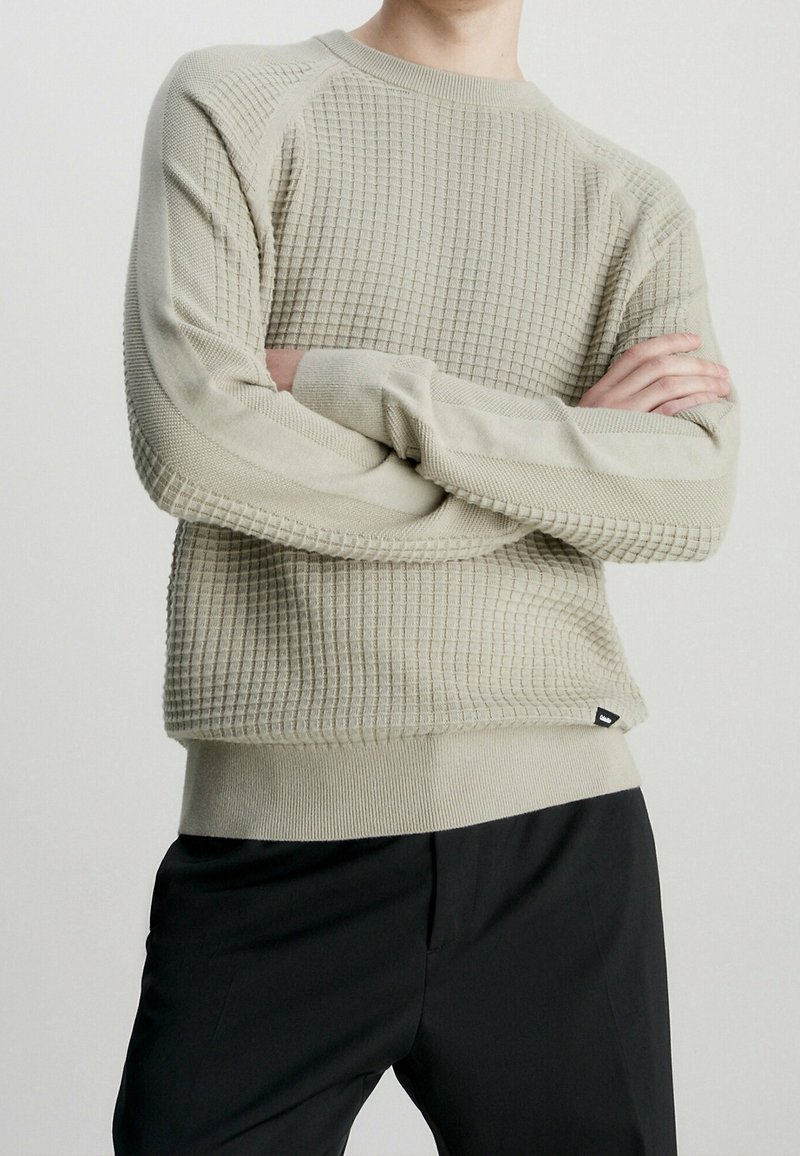 Hellgrauer strukturierter Pullover mit Karomuster, gerippten Bündchen und Saum, rundem Ausschnitt und taillierter Silhouette. Schwarzes Logo-Label am Saum.