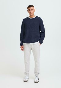 Marine gebreide trui met een ronde hals, grijze joggingsbroek en witte sneakers. De trui heeft een gestructureerd patroon en een relaxte pasvorm.