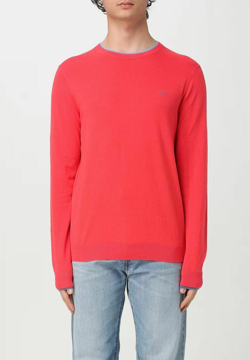 Maglione rosso con maniche lunghe, polsini e orlo a costine, scollatura rotonda bordata di azzurro chiaro, con un piccolo logo sul petto.