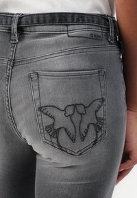 I jeans in denim grigio presentano un design aderente con un distintivo ricamo di uccello sulla tasca posteriore. Texture liscia con una finitura sbiadita.