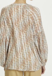 Blusa leggera e stampata con un mix di design geometrici marroni e blu, maniche lunghe a sbuffo e vestibilità ampia. Presenta una texture in tessuto morbido.
