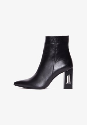 Bota de tobillo de cuero negro con punta afilada y un tacón cuadrado estructurado que presenta un corte rectangular transparente. Textura suave, diseño elegante.