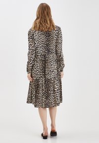 Långärmad, lager-på-lager klänning i leopardmönster med beige- och bruna nyanser, tillverkad av mjuk väv. Platta sandaler fulländar looken.