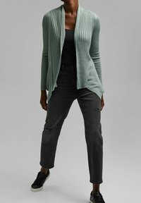 Vaaleanvihreä ribbineuloksinen neuletakki, jossa avoin etuosa, kerrostettuna mustan paidan päälle. Yhdistetty kuluneisiin mustiin farkkuihin ja mustiin tennareihin.